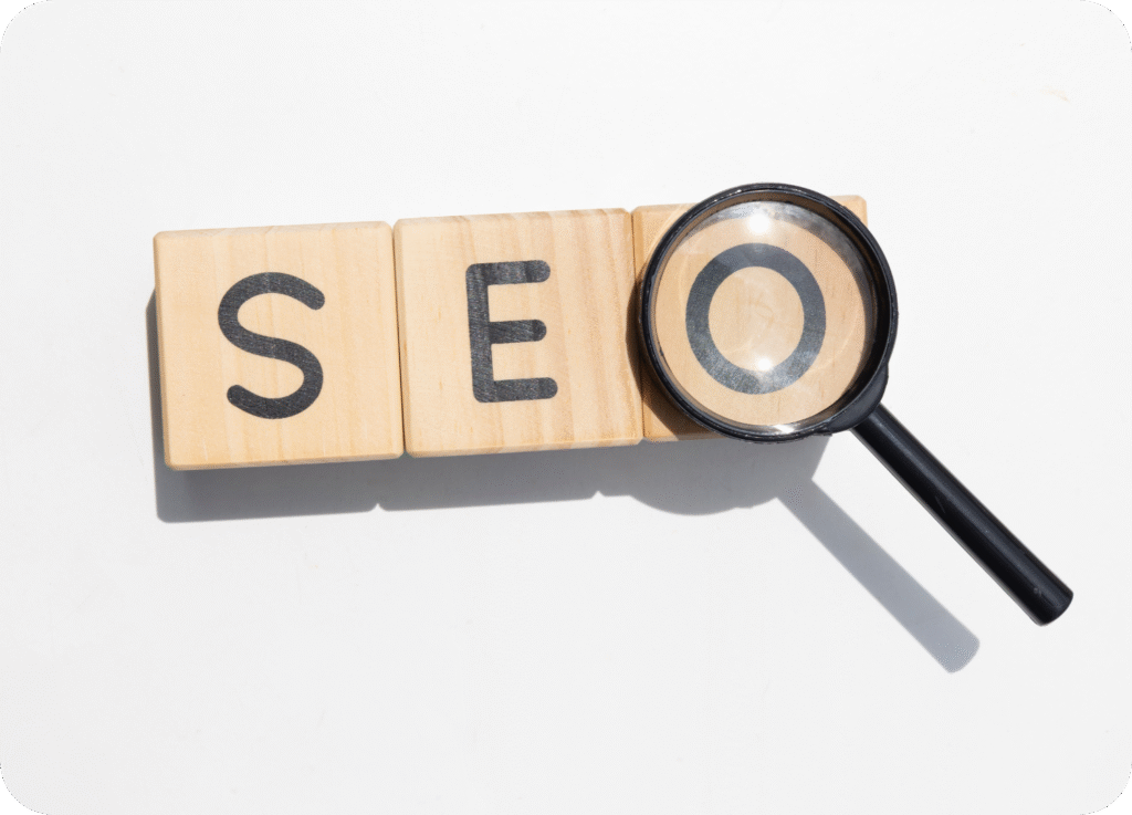 Blocos de madeira formando a sigla SEO, com uma lupa amplificando a letra O. A imagem simboliza a otimização de sites e a busca por resultados.