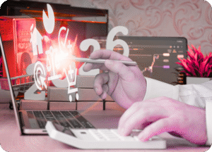 Mãos calculando em uma calculadora sobre um laptop. A tela mostra o número "26" e ícones digitais (e-commerce, casa, gráficos) projetados como se estivessem saindo da tela, simbolizando as tendências de marketing digital de 2026 e a otimização de custos.