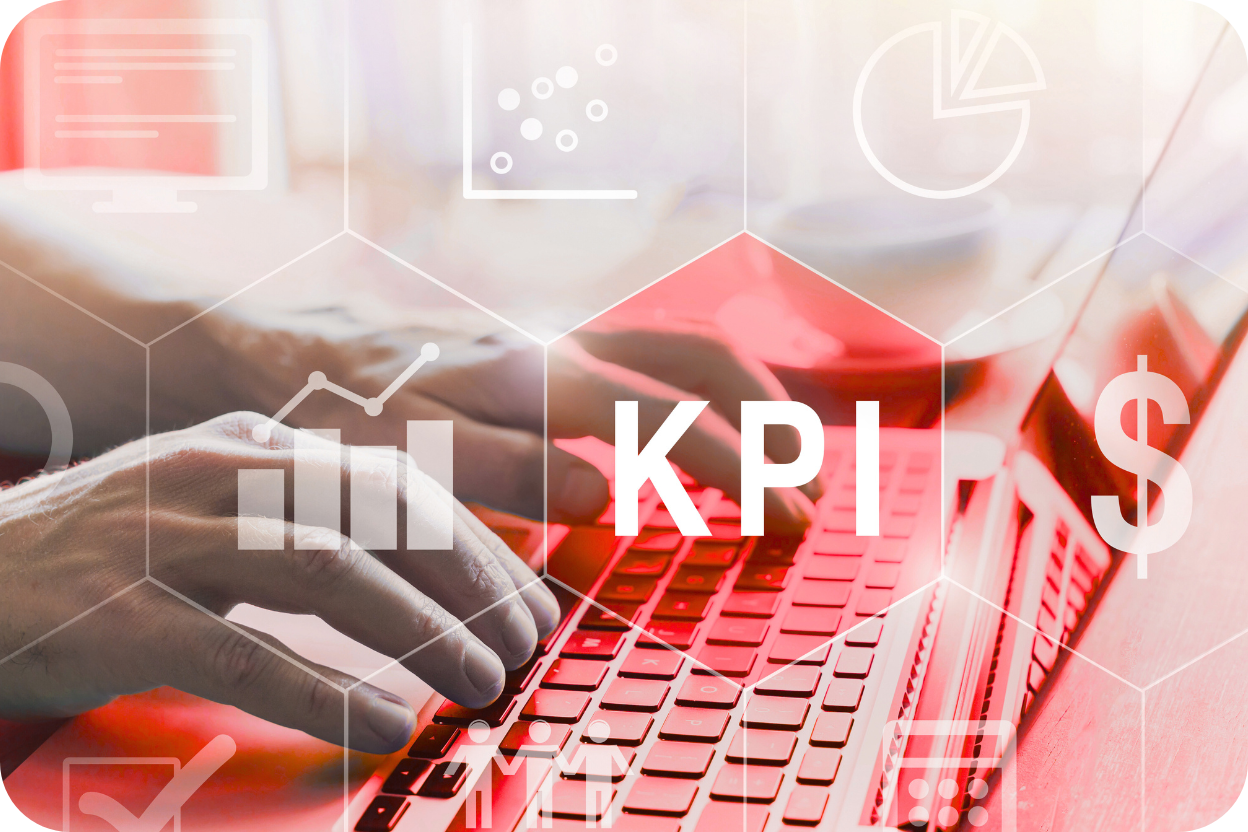 Mãos digitando em um laptop com uma sobreposição gráfica futurista em tons de vermelho, destacando um hexágono com a sigla KPI (Key Performance Indicator) no centro. O gráfico inclui ícones de análise de dados, gráficos de barras e um símbolo de dólar ($), representando o uso de métricas financeiras e de desempenho.