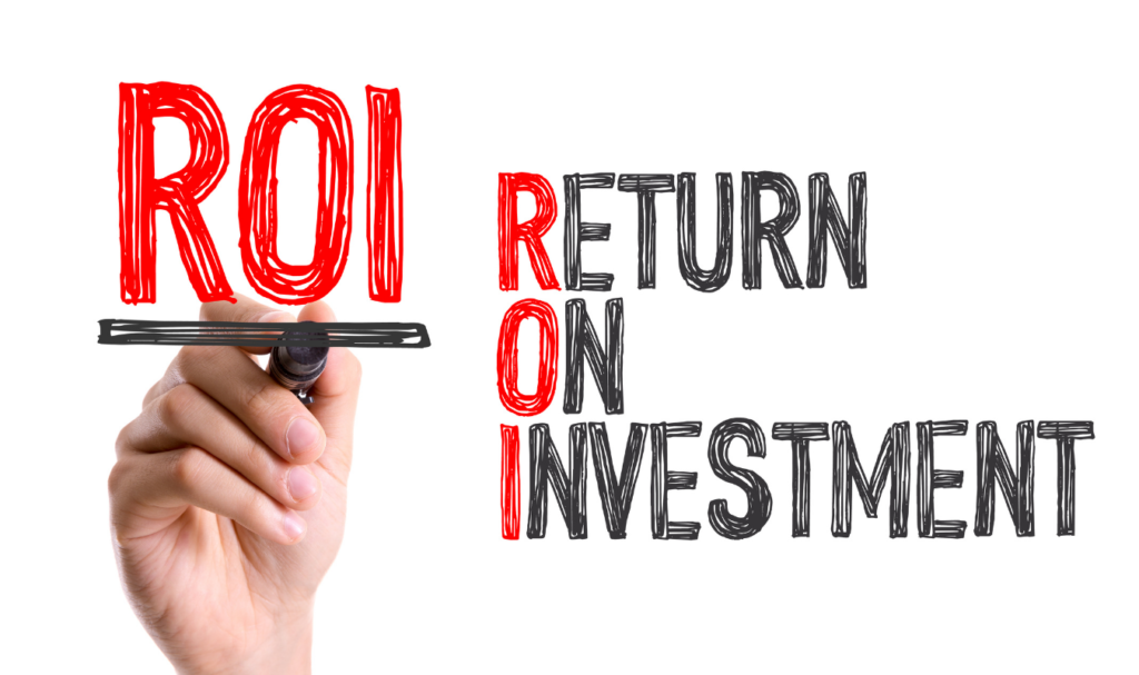 Uma mão segura uma caneta hidrográfica preta e escreve a sigla 'ROI' em letras grandes e vermelhas sobre um fundo branco. Ao lado, o significado 'Return on Investment' é escrito verticalmente em preto, com as iniciais destacadas em vermelho. A imagem simboliza a análise de rentabilidade, a métrica de sucesso de campanhas publicitárias e o foco em resultados financeiros reais.
